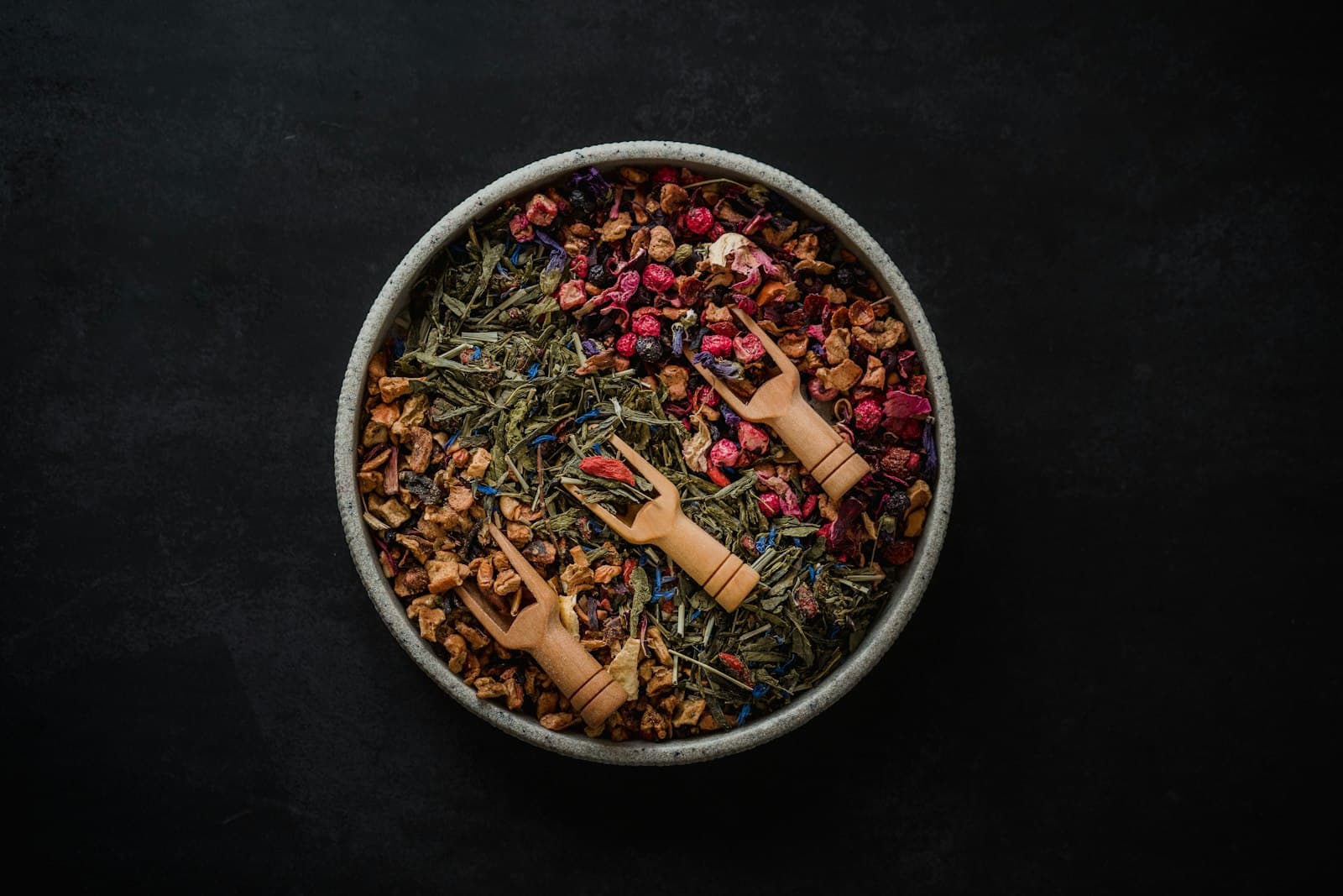 A bowl of loose-leaf herbal tea with wooden scoops