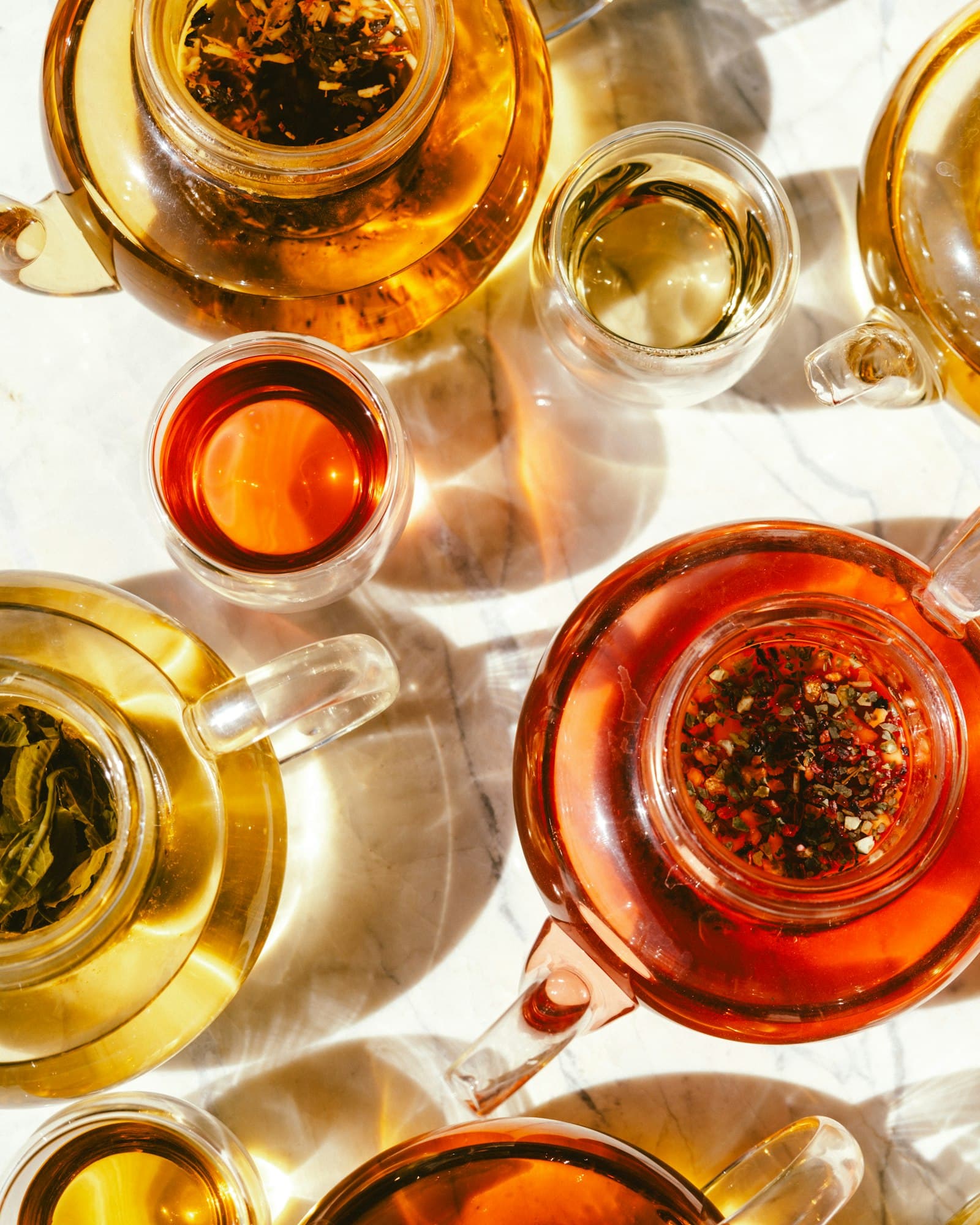 Several teas brewing in glass pots and cups, seen from above